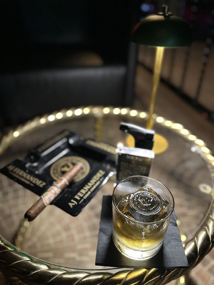 Bandeja de plata con un cigarro, un whisky y el encendedor bajo la lampara de mesa