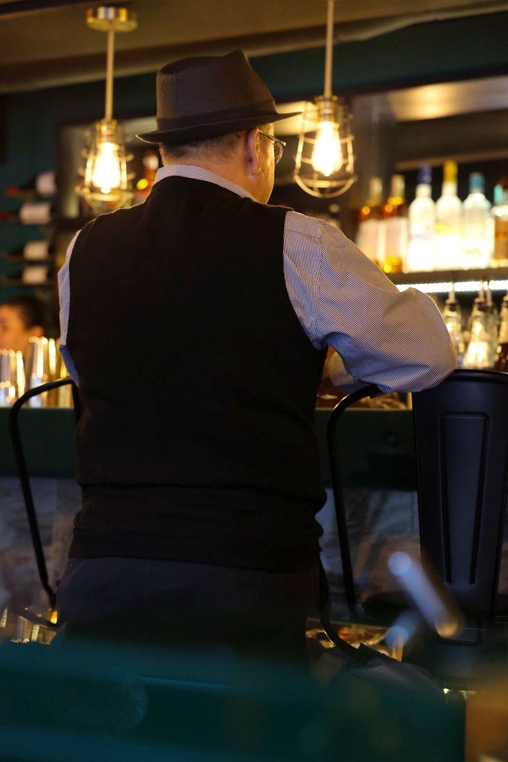 El bartender trabajando detras de la barra, con la estanteria iluminada por detras